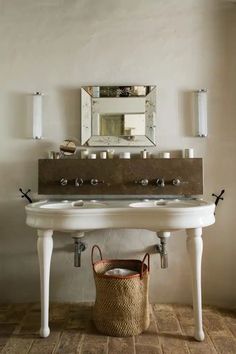 a bathroom sink sitting under a mirror next to a basket with candles on top of it