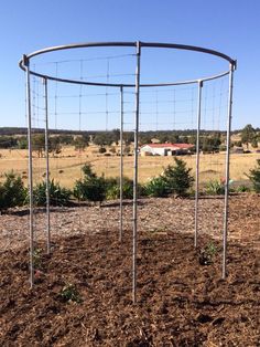 a metal circular structure in the middle of a field with dirt and grass around it