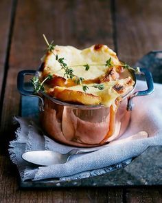 a casserole dish with cheese and herbs in it sitting on a napkin next to a spoon