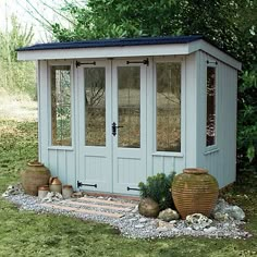 a small garden shed with two large vases on the ground in front of it