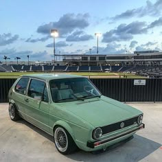 a green car parked in front of a baseball field