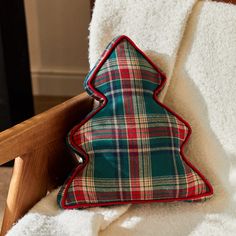 a plaid christmas tree pillow sitting on top of a white blanket next to a wooden chair