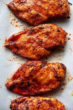 three pieces of chicken sitting on top of a piece of parchment paper covered in seasoning