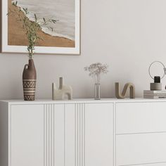 a white cabinet with vases and flowers on it in front of a framed painting