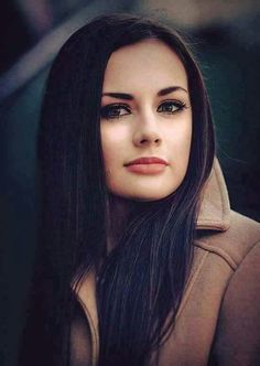 a woman with long black hair wearing a coat