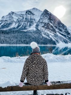 a person sitting on a bench in the snow looking out over a lake and mountains