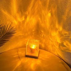 a lit candle sitting on top of a table next to a palm leaf and wall