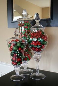 two glass vases filled with christmas ornaments on top of a black table next to a mirror