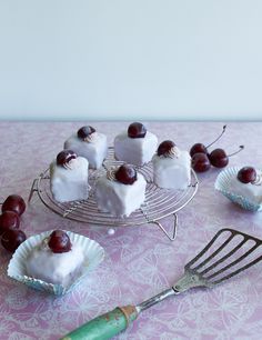 small desserts with cherries and whipped cream on a wire rack next to a spatula