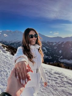 a woman holding the hand of a man on top of a snow covered mountain