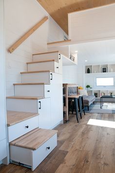 a living room with stairs leading up to the top floor and kitchen in the background