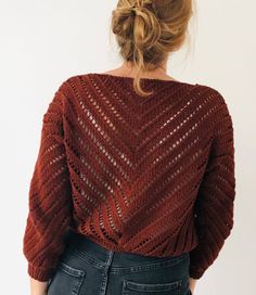 a woman wearing a red sweater and jeans with her back to the camera, looking down