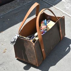 a brown leather bag filled with pens, pencils and other office supplies sitting on the ground