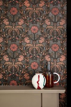 a vase sitting on top of a wooden table next to a wallpapered wall