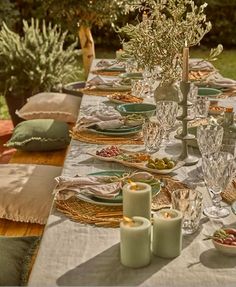 a table set with plates, candles and napkins for an outdoor dinner party in the garden