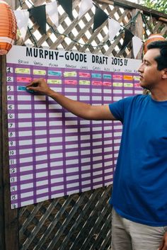 a man standing next to a purple and white calendar on a wooden fence with paper lanterns hanging from it