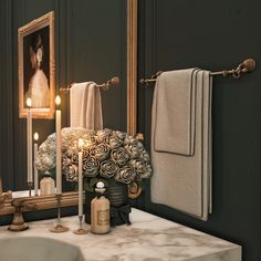 a bathroom with green walls and marble counter top, candles on the sink and towels hanging above it