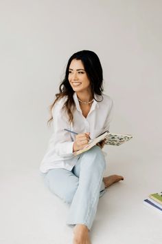 a woman sitting on the floor holding a book and smiling at the camera with her legs crossed