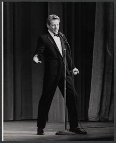 a black and white photo of a man in a tuxedo singing into a microphone