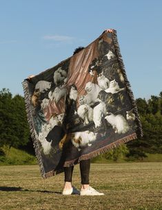 a person standing in a field holding up a blanket with pictures of cats on it