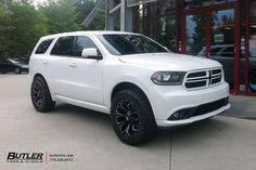 a white dodge suv is parked in front of a building with black rims and tires