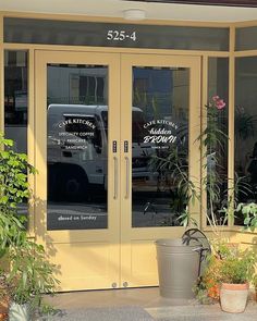 a couple of plants that are sitting in front of a building with some glass doors