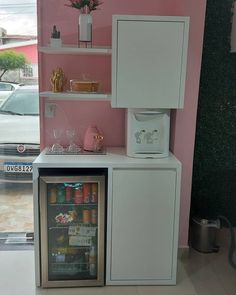 a mini fridge is in front of a pink wall with shelves and glassware on it