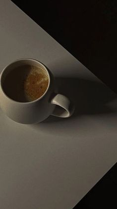 a cup of coffee sitting on top of a white table next to a black wall