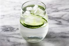 a glass filled with ice and cucumber on top of a marble countertop