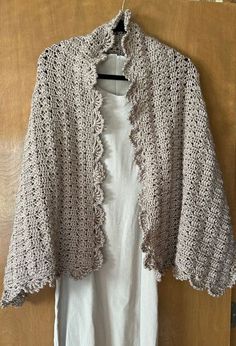 a crocheted jacket hanging on a wooden door with a white shirt underneath it