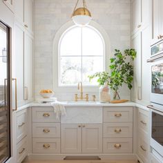 a kitchen with white cabinets and gold hardware on the countertops, along with an arched window