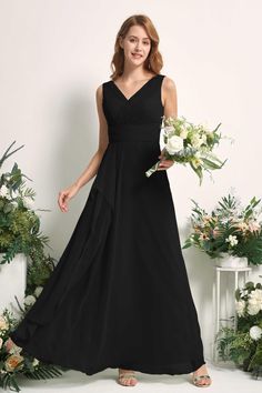 a woman wearing a black bridesmaid dress standing in front of flowers and greenery