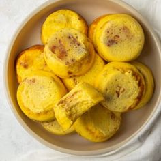 a white bowl filled with yellow desserts on top of a white table cloth next to a cup of coffee