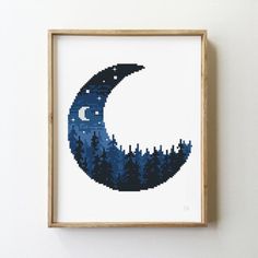 a cross - stitch picture of the moon and trees is hanging in a frame on a wall