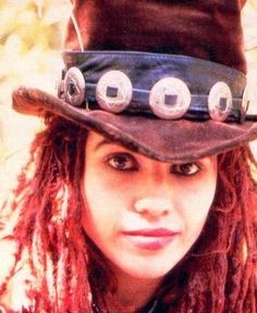 a woman wearing a hat with buttons and chains on it's side, looking at the camera