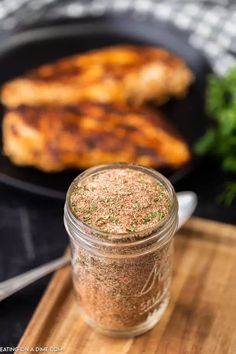 a close up of a jar of seasoning next to chicken on a cutting board