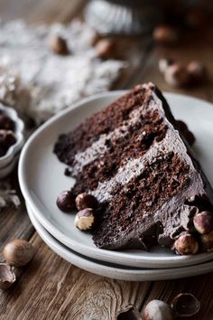 a piece of chocolate cake on a plate with nuts around it and another slice in the background