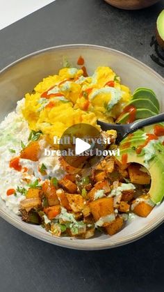 a bowl filled with rice and vegetables on top of a black counter next to an avocado