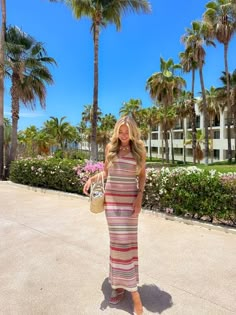 a woman is standing in front of palm trees and holding a basket with her hand