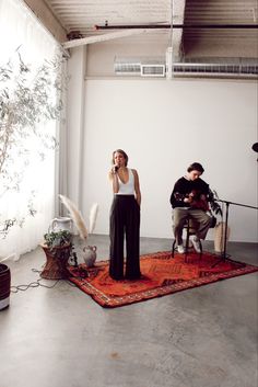 a woman standing on top of a rug next to a man sitting in a chair