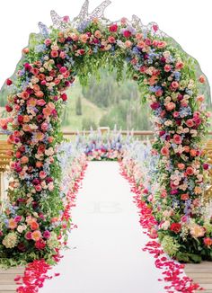 an archway decorated with flowers and leaves for a wedding ceremony at the end of a long aisle