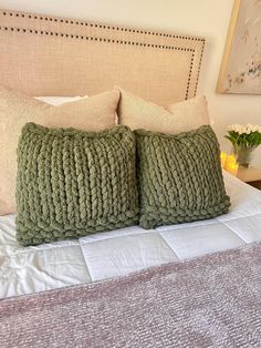 two green knitted pillows sitting on top of a bed next to a night stand