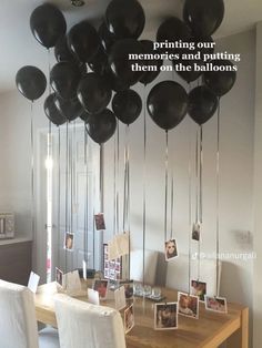 black balloons are hanging from the ceiling above a dining room table with white chairs and pictures on it