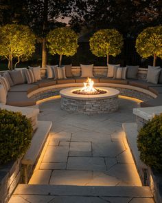 an outdoor fire pit surrounded by seating and trees at night with lights shining on it