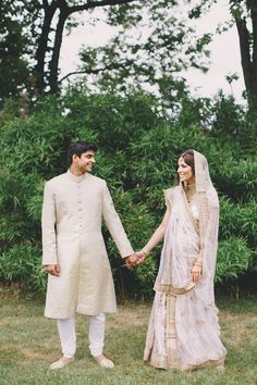 a bride and groom holding hands while standing in the grass with trees behind them on their wedding day