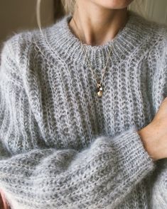 a woman wearing a gray sweater is holding her hands on her chest and looking at the camera