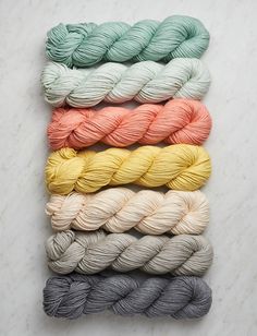 six skeins of yarn in different colors on a marble surface with text overlay