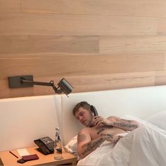 a man laying in bed while talking on his cell phone with tattoos on his arm