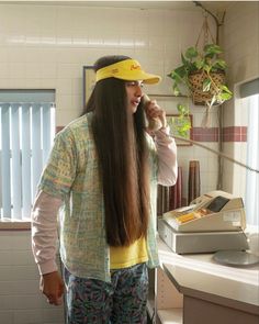 a woman with long hair is talking on the phone and wearing a hat while standing in front of a counter