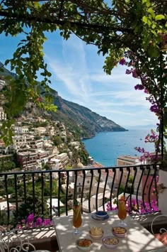 an outdoor table with two plates of food on it overlooking the ocean and town below